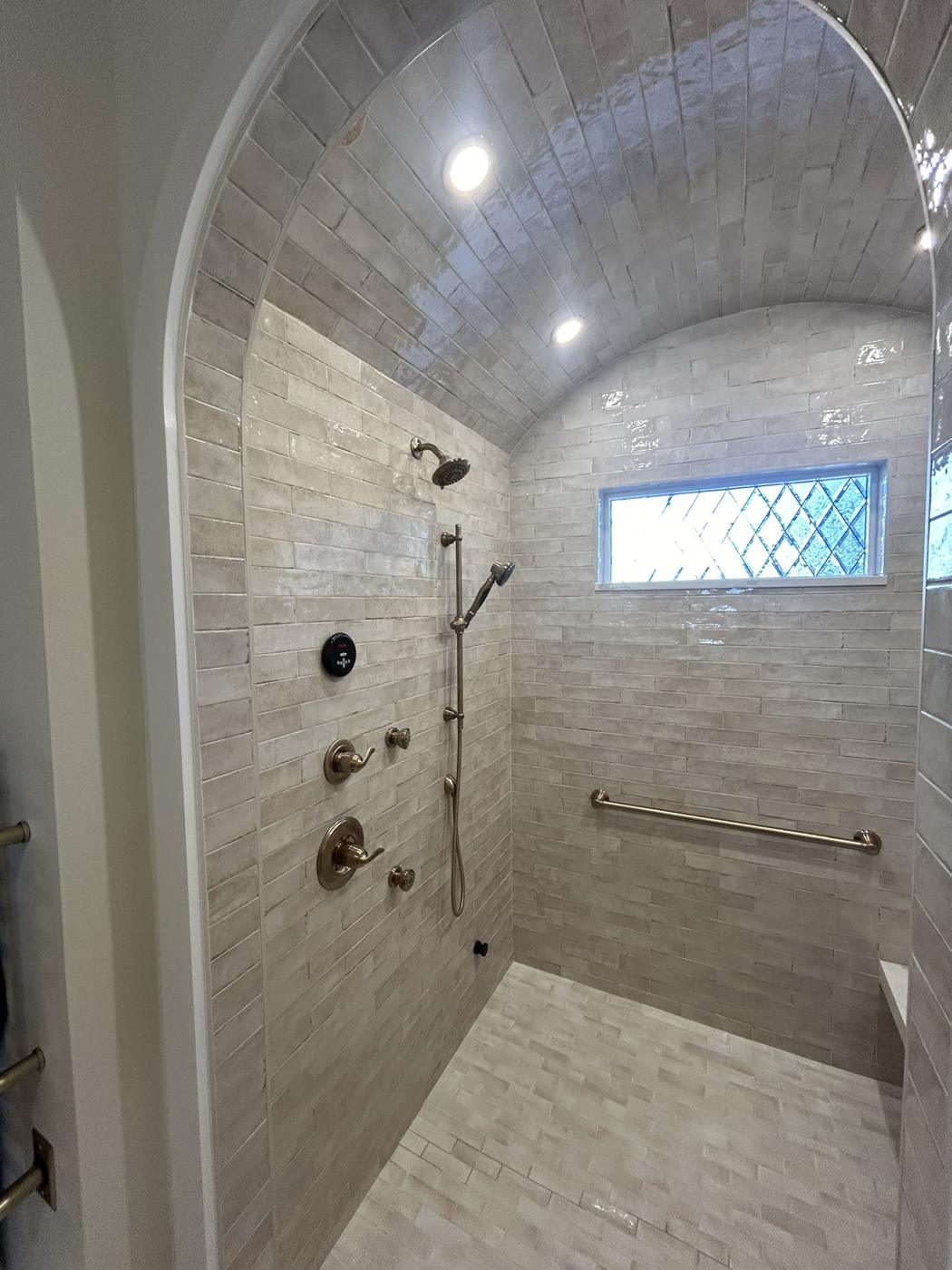 Arched walk-in shower with large-format tile, bench and window
